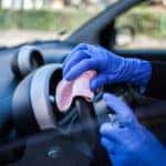 Close up of person wiping down steering wheel wearing blue rubber gloves.