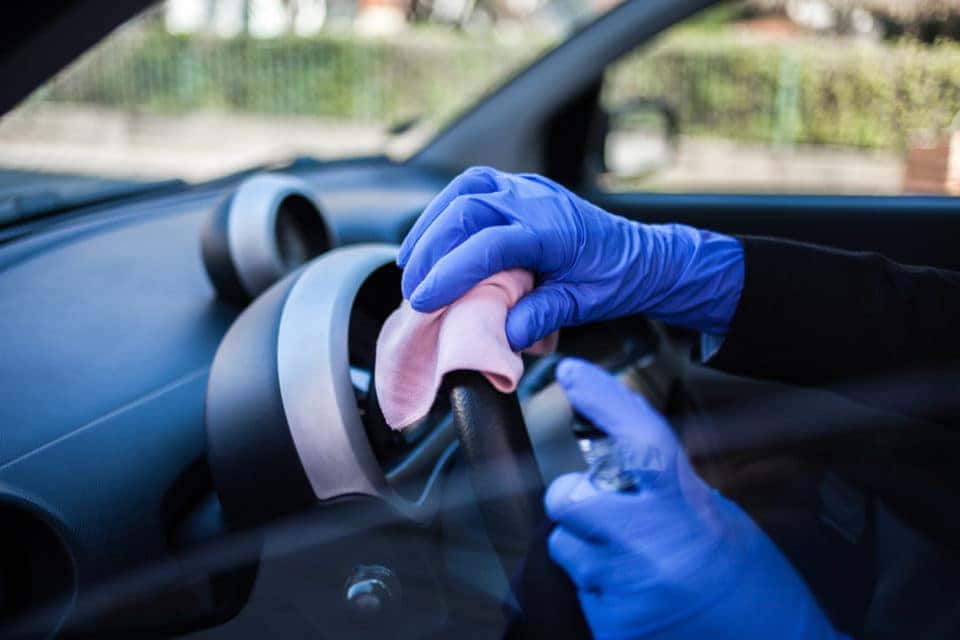 Close up of person wiping down steering wheel wearing blue rubber gloves.