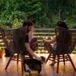 A couple sitting on their porch in rattan chairs at sunset. Petting a cat.