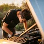 Young man looking under the hood of his vehicle